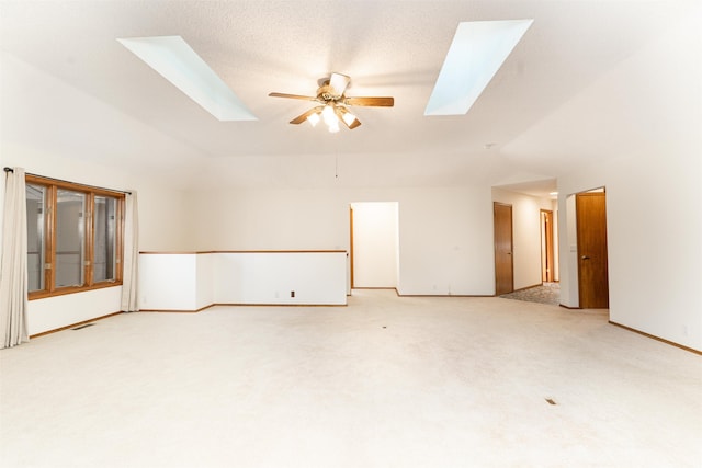 empty room featuring lofted ceiling with skylight, carpet floors, a textured ceiling, and ceiling fan