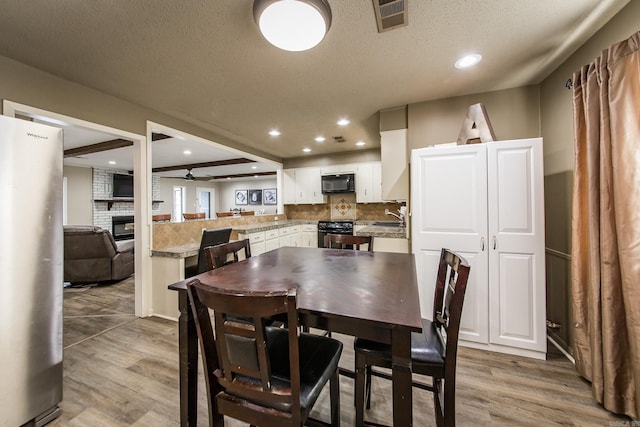 dining area featuring hardwood / wood-style flooring, ceiling fan, a brick fireplace, and a textured ceiling