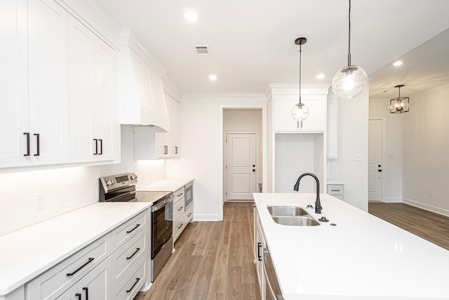 kitchen featuring decorative light fixtures, white cabinetry, sink, stainless steel appliances, and a center island with sink