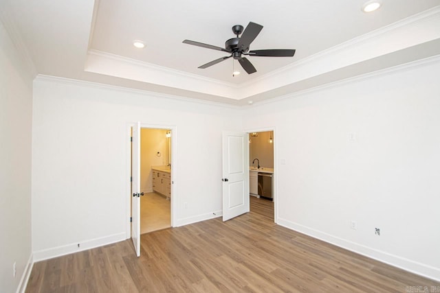 unfurnished bedroom with sink, a tray ceiling, ornamental molding, and light hardwood / wood-style floors