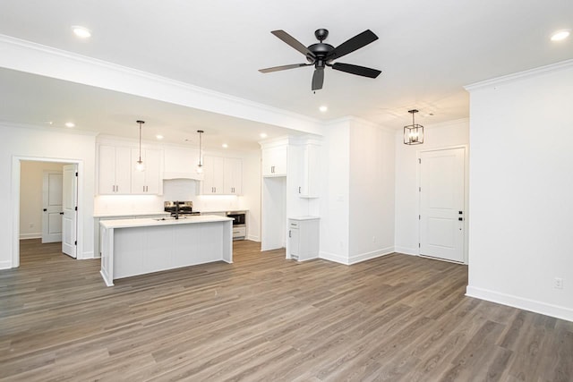 kitchen with pendant lighting, white cabinetry, ornamental molding, a center island with sink, and light wood-type flooring