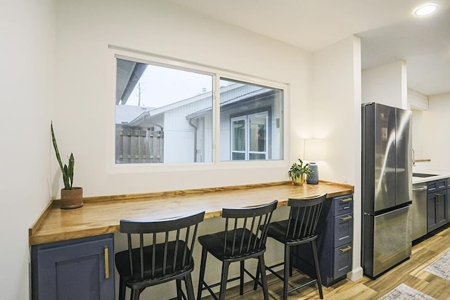 kitchen featuring stainless steel appliances, a breakfast bar, wood counters, and light hardwood / wood-style flooring
