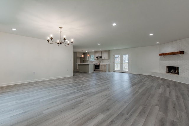 unfurnished living room with a brick fireplace, a notable chandelier, light hardwood / wood-style flooring, and french doors