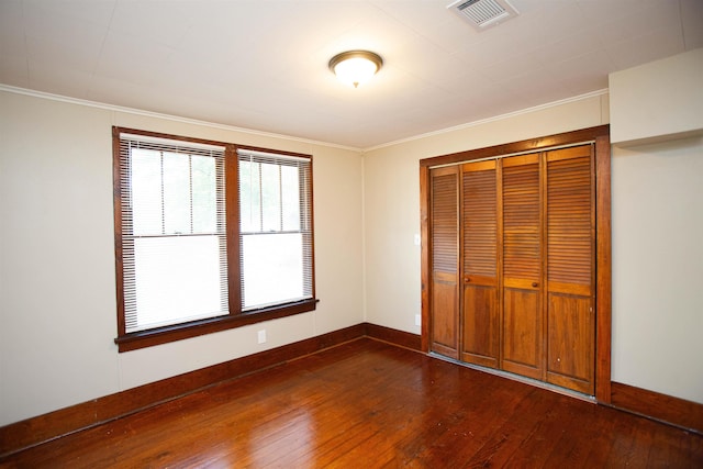 unfurnished bedroom with dark wood-type flooring, ornamental molding, and a closet