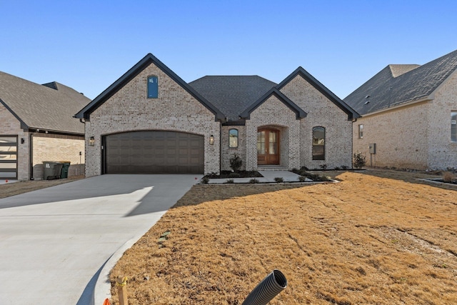 french country home featuring a garage, concrete driveway, and brick siding