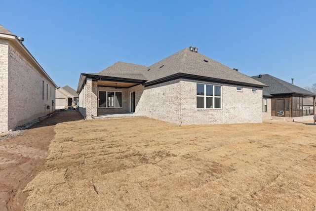 rear view of property with a yard, a shingled roof, and brick siding