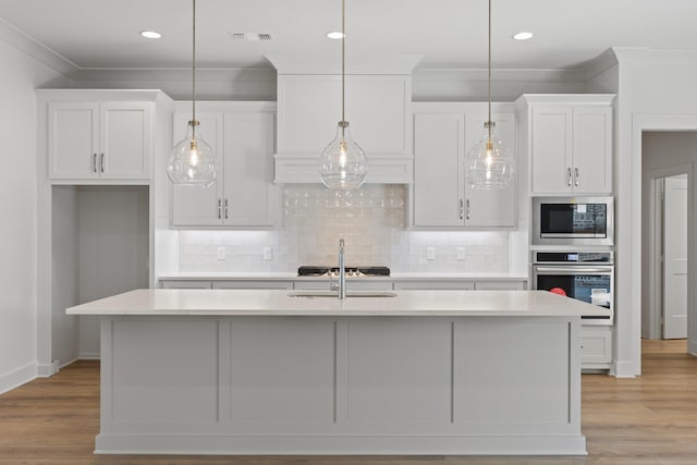 kitchen featuring pendant lighting, stainless steel appliances, light countertops, white cabinets, and an island with sink