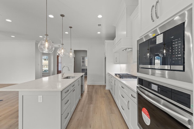 kitchen featuring stainless steel appliances, a sink, hanging light fixtures, light countertops, and an island with sink