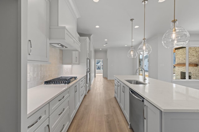 kitchen featuring decorative backsplash, appliances with stainless steel finishes, decorative light fixtures, a kitchen island with sink, and a sink