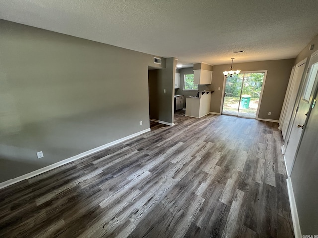 unfurnished living room with dark wood-type flooring, a textured ceiling, and a notable chandelier