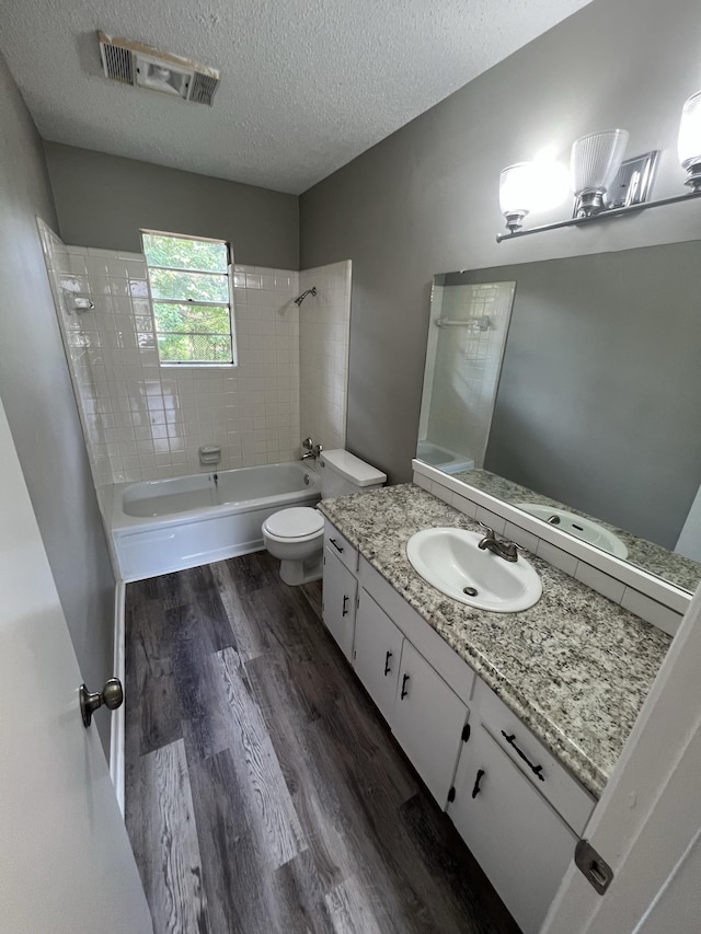 full bathroom featuring hardwood / wood-style floors, vanity, a textured ceiling, tiled shower / bath, and toilet