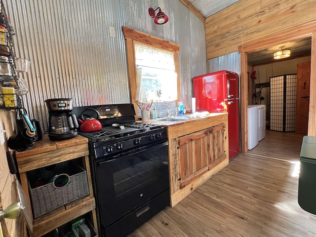 kitchen with independent washer and dryer, sink, gas stove, and light wood-type flooring