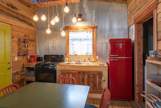 kitchen with sink, wood walls, decorative light fixtures, black gas stove, and hardwood / wood-style floors