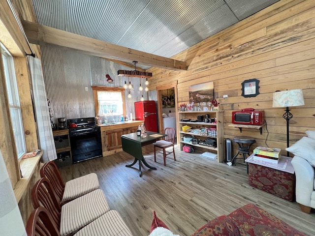 interior space featuring vaulted ceiling with beams, hanging light fixtures, fridge, hardwood / wood-style flooring, and black gas range