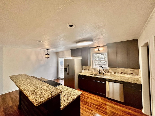 kitchen featuring sink, hanging light fixtures, appliances with stainless steel finishes, a kitchen island, and light stone countertops