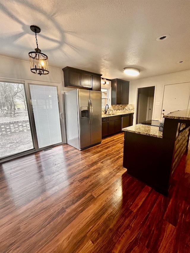 kitchen featuring dark brown cabinets, dark hardwood / wood-style floors, stainless steel fridge, pendant lighting, and light stone countertops