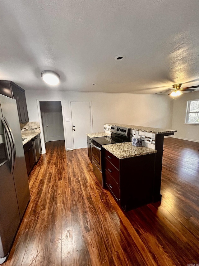kitchen with stainless steel appliances, a center island, light stone countertops, a textured ceiling, and dark hardwood / wood-style flooring