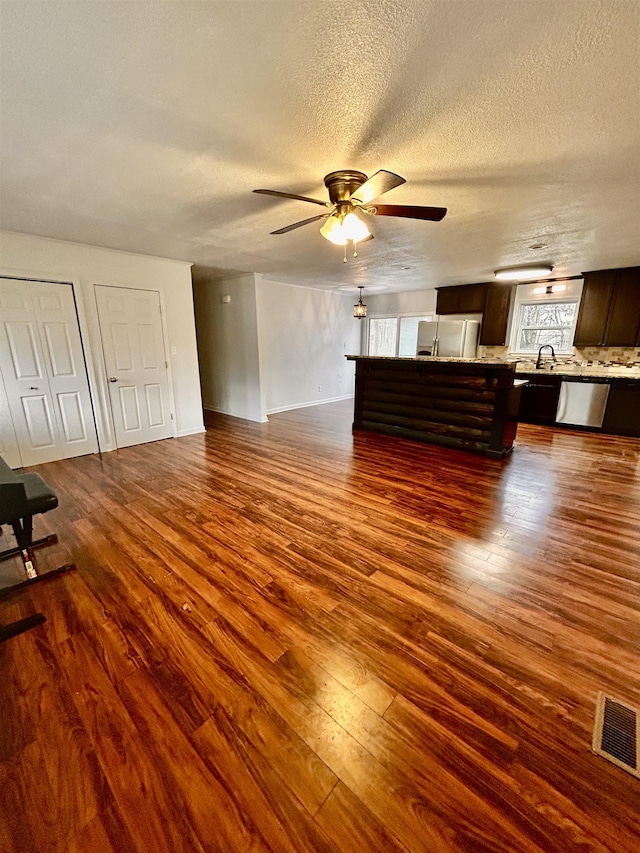 unfurnished living room featuring dark hardwood / wood-style flooring, sink, a textured ceiling, and ceiling fan