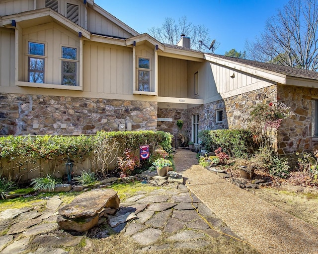 view of front of home with stone siding, a chimney, and board and batten siding