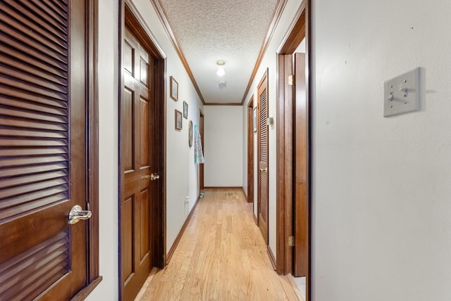 hall featuring ornamental molding, light wood-type flooring, and a textured ceiling