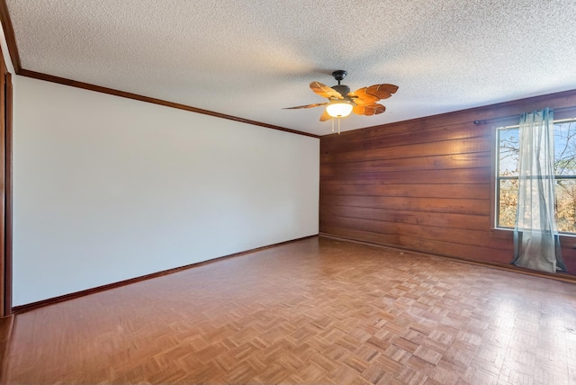 spare room featuring wood walls, light parquet floors, ornamental molding, ceiling fan, and a textured ceiling