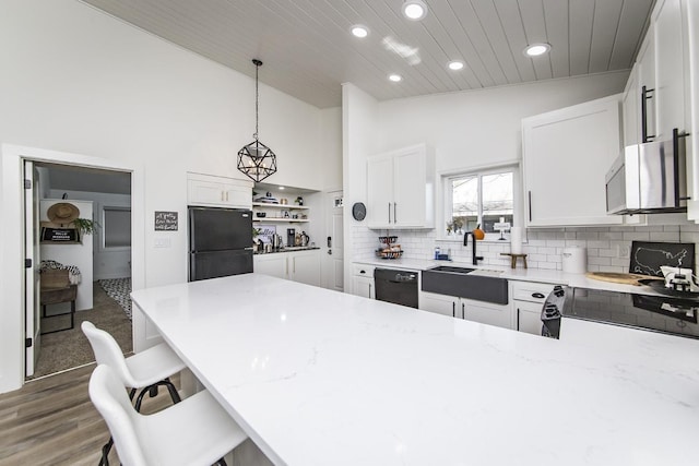 kitchen with a breakfast bar, sink, pendant lighting, light stone countertops, and black appliances