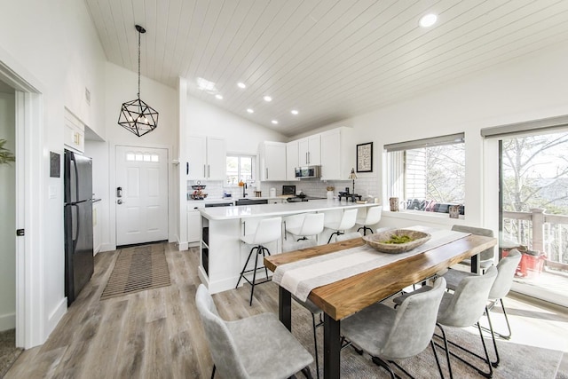 dining room featuring high vaulted ceiling, sink, wood ceiling, and light hardwood / wood-style flooring