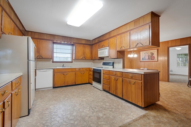 kitchen featuring sink, white appliances, a textured ceiling, kitchen peninsula, and wood walls