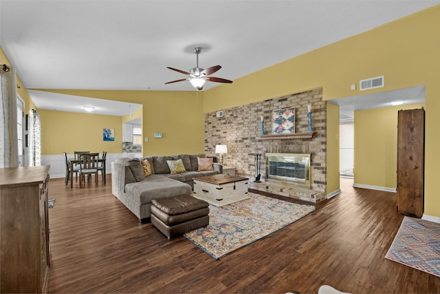 living room featuring a brick fireplace, dark wood-type flooring, lofted ceiling, and ceiling fan