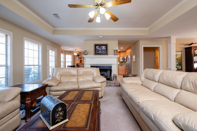 carpeted living room featuring a raised ceiling, ornamental molding, ceiling fan, and a fireplace