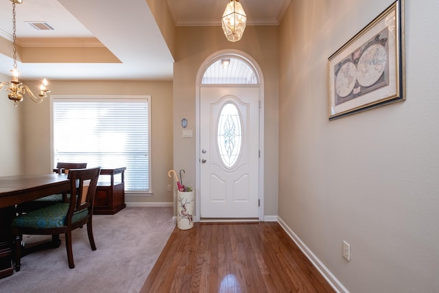 foyer entrance with an inviting chandelier, ornamental molding, plenty of natural light, and a tray ceiling