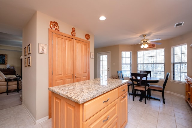 kitchen featuring light stone countertops, light tile patterned floors, a kitchen island, and light brown cabinets