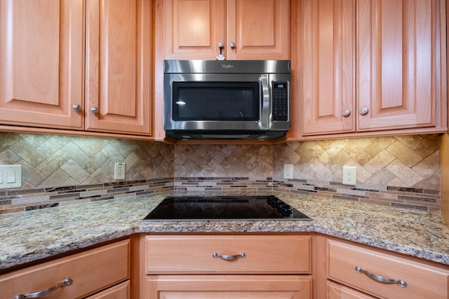 kitchen featuring black electric stovetop, backsplash, and light stone counters