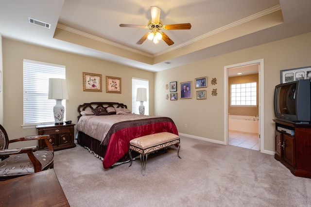 bedroom with crown molding, a tray ceiling, light colored carpet, and ensuite bathroom