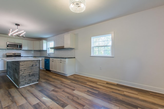 kitchen with appliances with stainless steel finishes, hanging light fixtures, tasteful backsplash, white cabinets, and dark hardwood / wood-style flooring