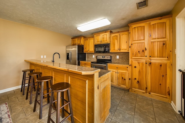 kitchen featuring sink, a kitchen breakfast bar, dark tile patterned flooring, stainless steel appliances, and decorative backsplash