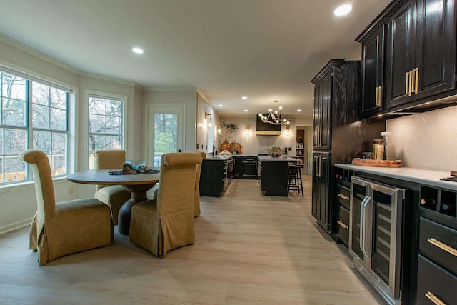 dining space featuring crown molding, indoor wet bar, beverage cooler, and light hardwood / wood-style flooring