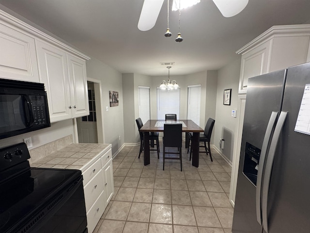 kitchen with black appliances, light tile patterned floors, tile counters, pendant lighting, and white cabinets