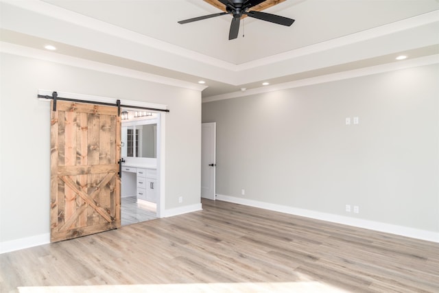 unfurnished room featuring light hardwood / wood-style flooring, ornamental molding, a tray ceiling, ceiling fan, and a barn door