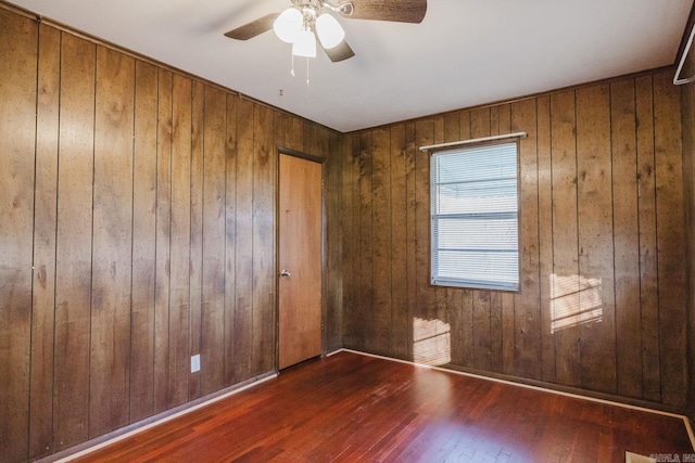 unfurnished room with wooden walls, ceiling fan, and dark hardwood / wood-style flooring