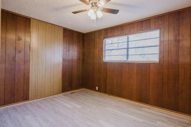 empty room with ceiling fan, wooden walls, a textured ceiling, and light hardwood / wood-style floors