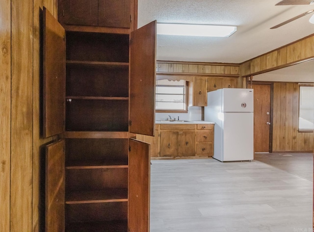 kitchen with sink, ceiling fan, wood walls, white fridge, and light wood-type flooring