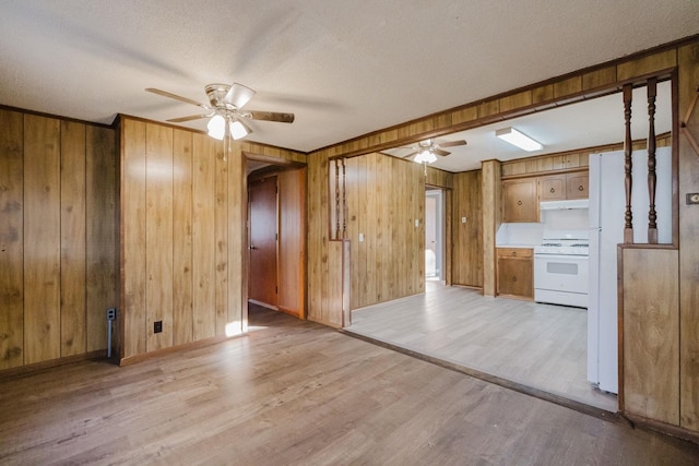 unfurnished living room featuring ceiling fan, wood walls, light hardwood / wood-style flooring, and a textured ceiling