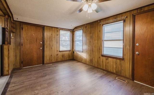 interior space with a textured ceiling, dark wood-type flooring, wooden walls, and ceiling fan