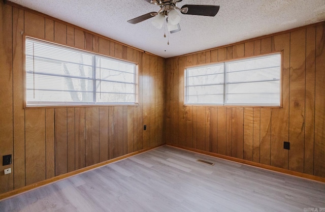 spare room with wooden walls, a textured ceiling, and light wood-type flooring