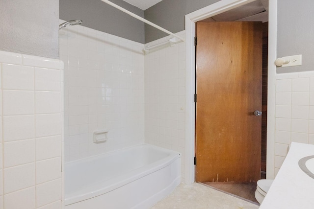 bathroom with tiled shower / bath, toilet, and tile walls