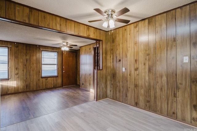 empty room with ceiling fan, wooden walls, a textured ceiling, and light hardwood / wood-style flooring