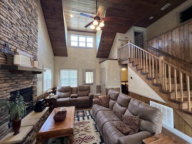 living room with wood ceiling, ceiling fan, a stone fireplace, and a towering ceiling