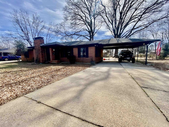 view of front facade featuring a carport, a chimney, concrete driveway, and brick siding