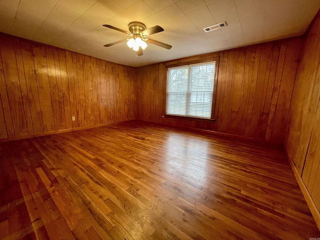 unfurnished room with hardwood / wood-style floors, wooden walls, and ceiling fan